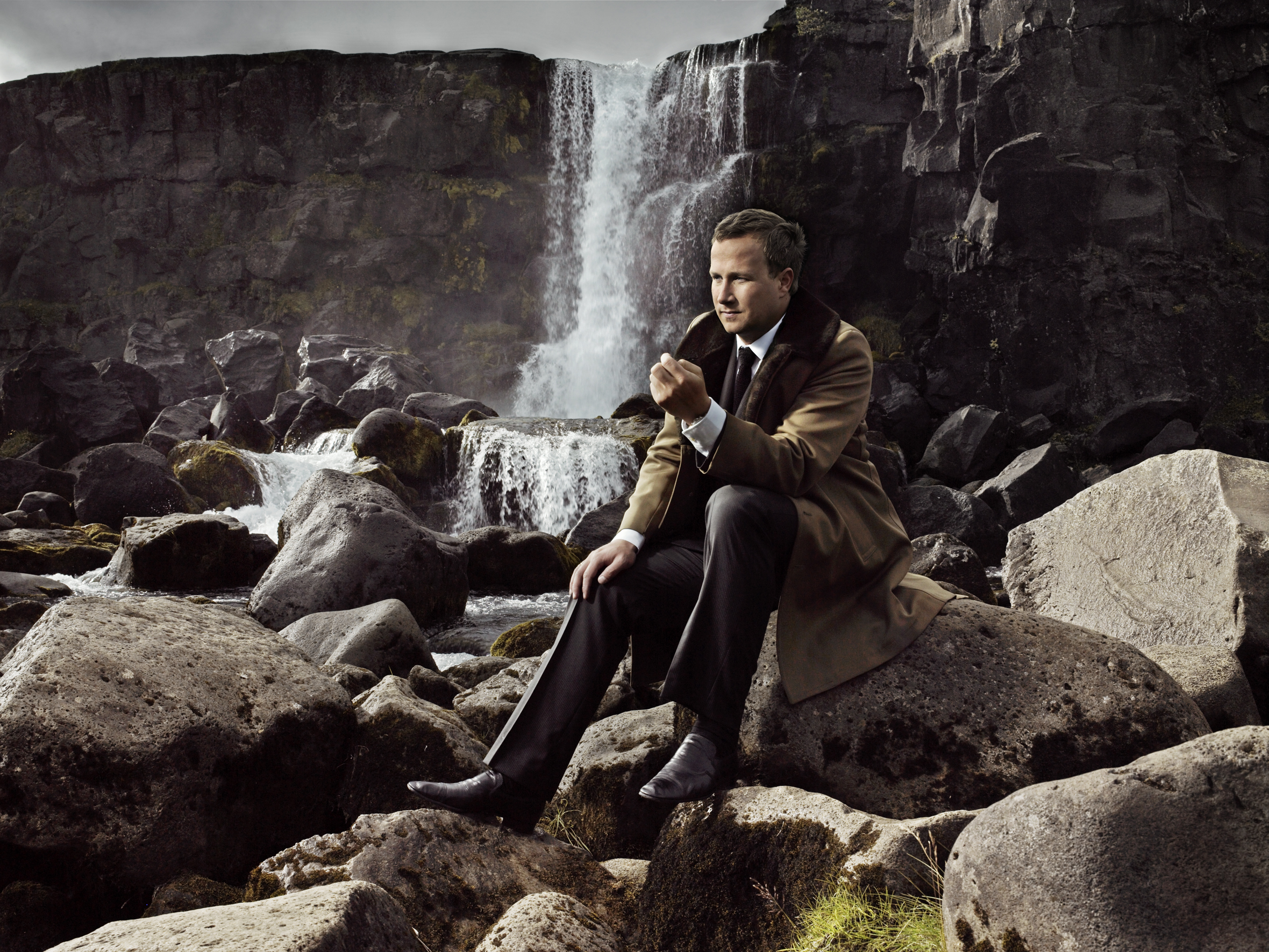 Andri Snær Magnason sitting on a rock in front of a waterfall